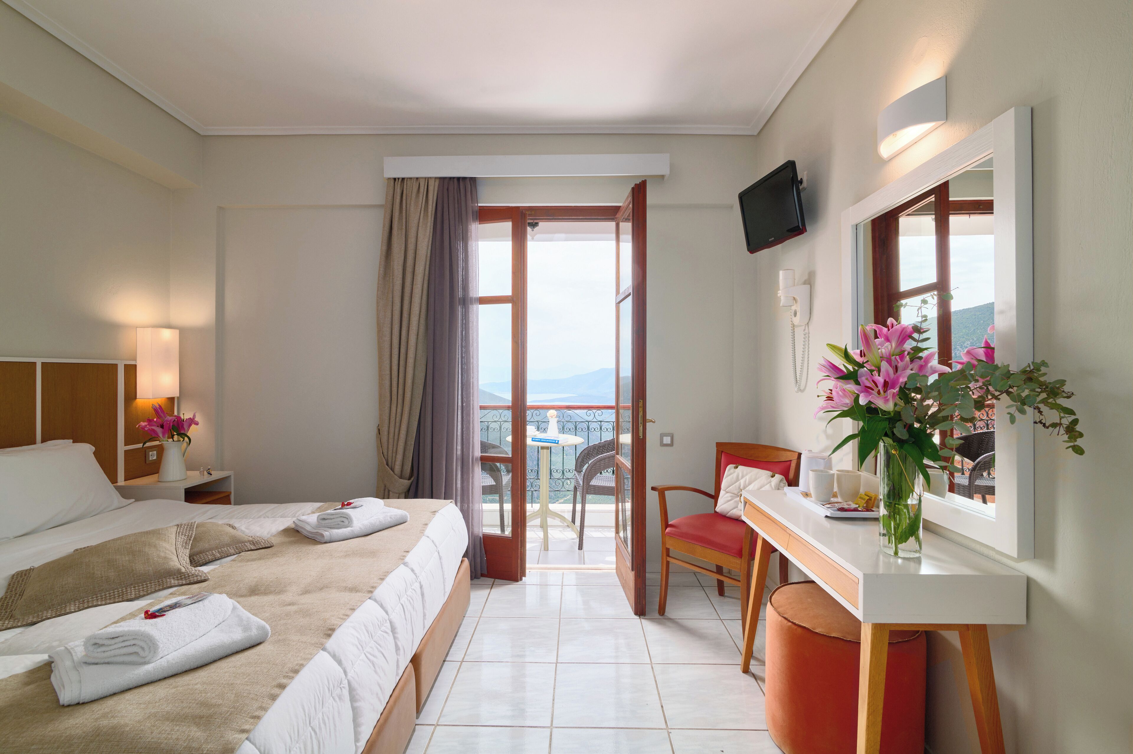 Habitación de hotel con cama, escritorio, silla, televisor y balcón con vistas.