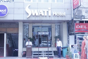 Exterior del Hotel Swati, con entrada despejada, un atril y una persona de pie, y un cartel sobre la entrada.