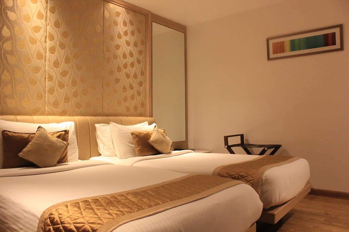 A hotel room with a large bed, a headboard with a leaf pattern, a mirror, and a framed picture on the wall.