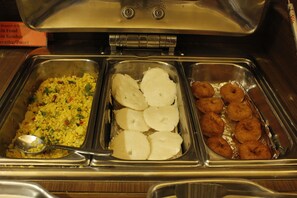 Un bufé con diversos alimentos, incluyendo arroz, rebanadas blancas y rosquillas fritas.