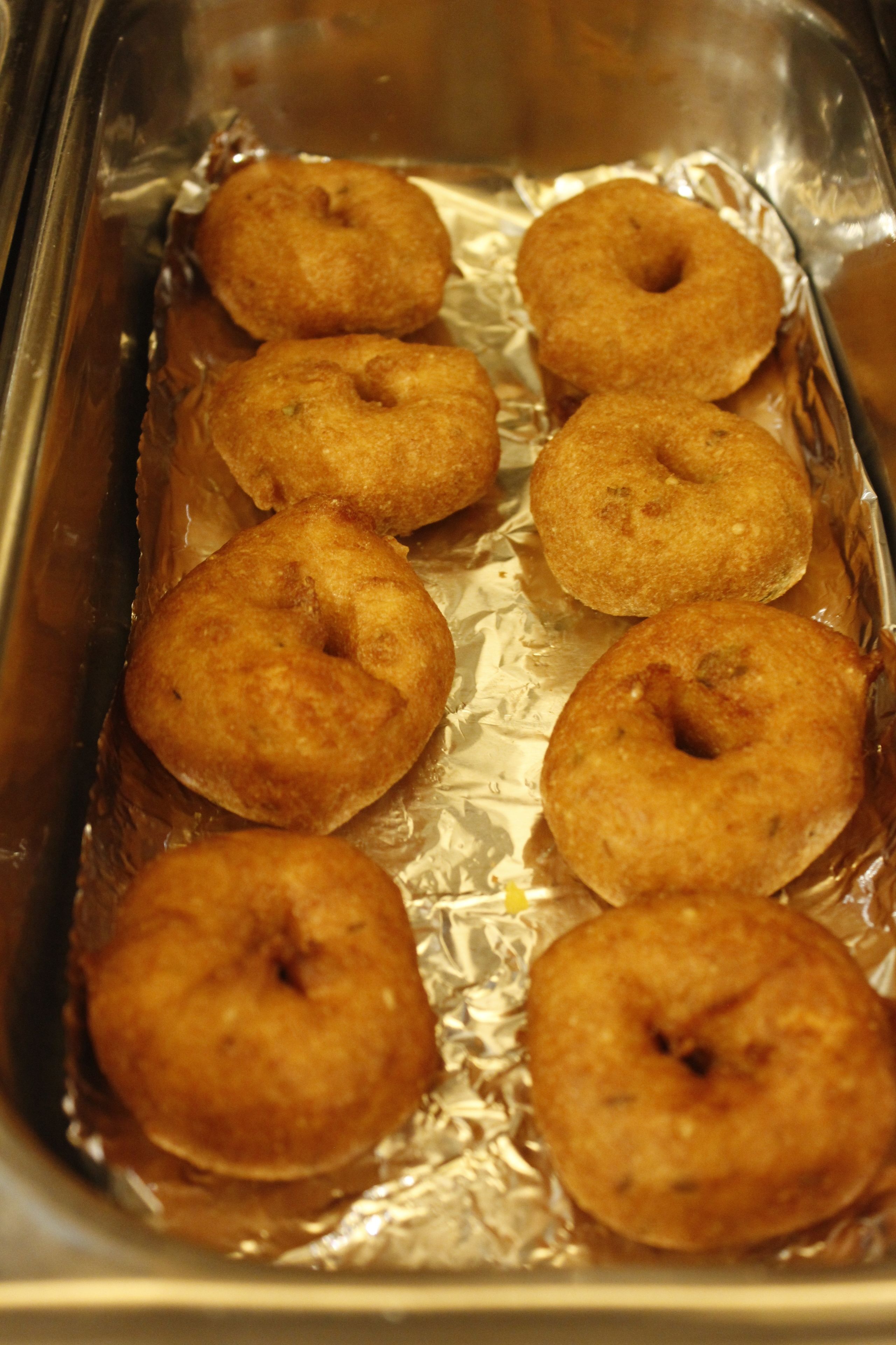 A tray of six golden-brown donuts on aluminum foil.
