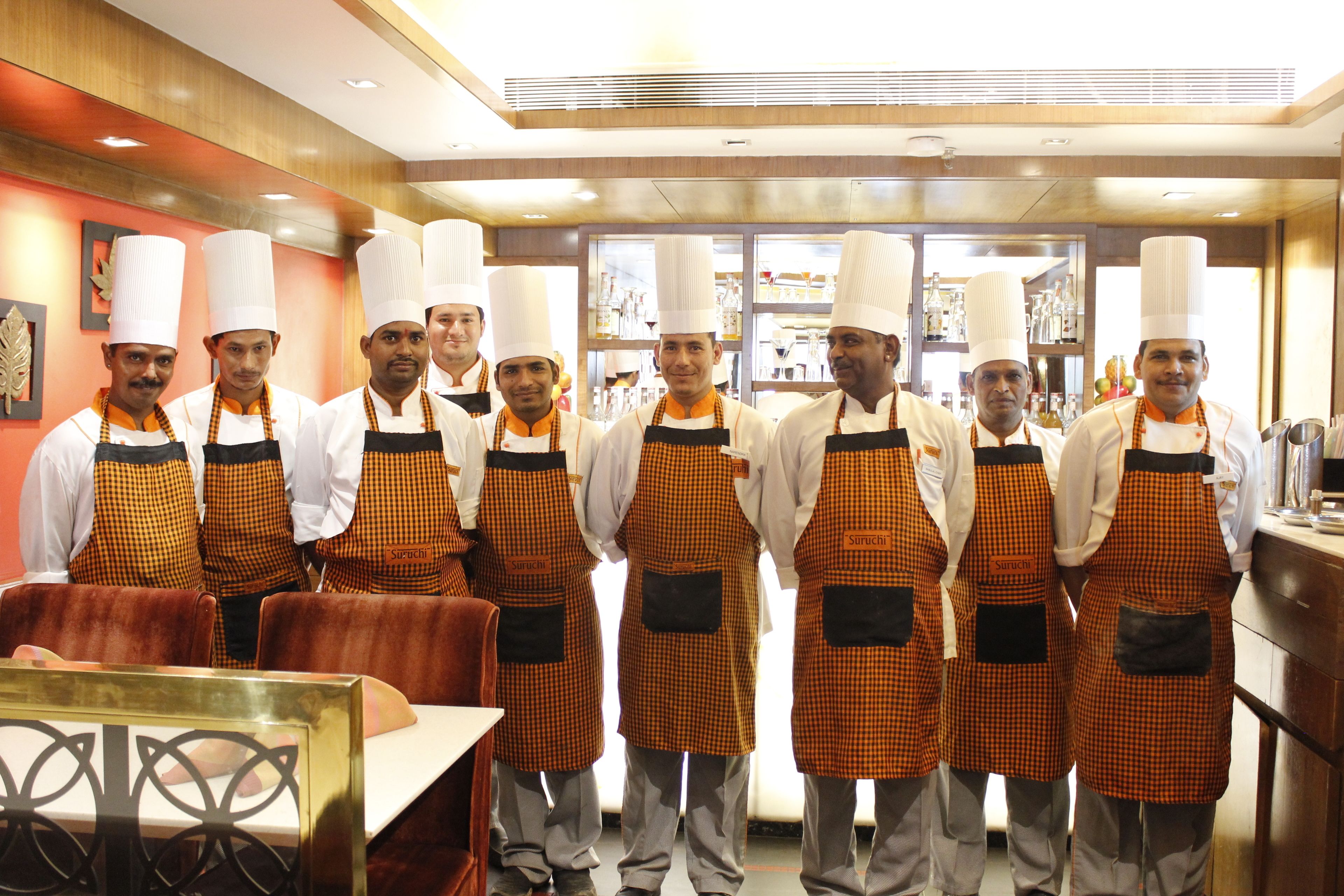 A group of chefs in a kitchen with wooden paneling and stainless steel appliances.