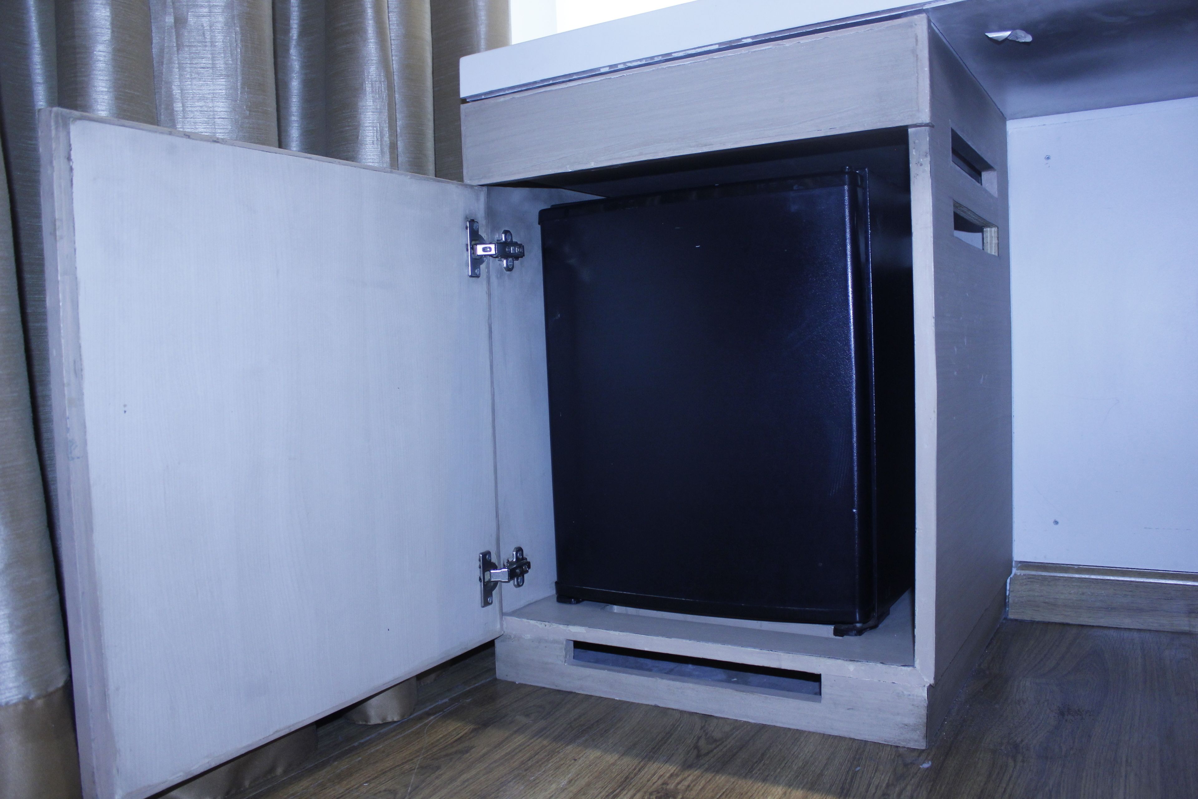 A compact, modern room with a built-in black safe, a wooden floor, and a white door.