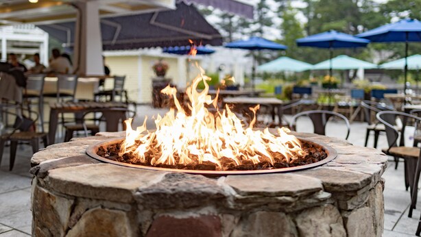 A stone fire pit with flames in an outdoor dining area. - The Admiral's Inn Resort (Ogunquit)