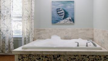 A bathroom with a mosaic-tiled sink area, a painting of a boat on a dock, and a window with floral curtains.
