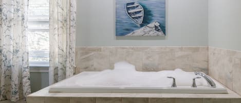 A bathroom with a mosaic-tiled sink area, a painting of a boat on a dock, and a window with floral curtains.