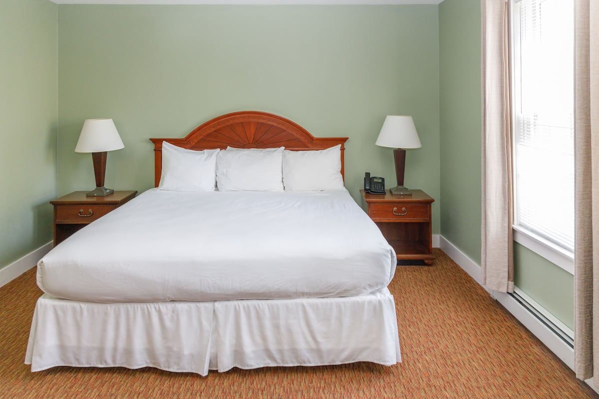A hotel room with a large bed, two bedside tables with lamps, and a window with curtains.