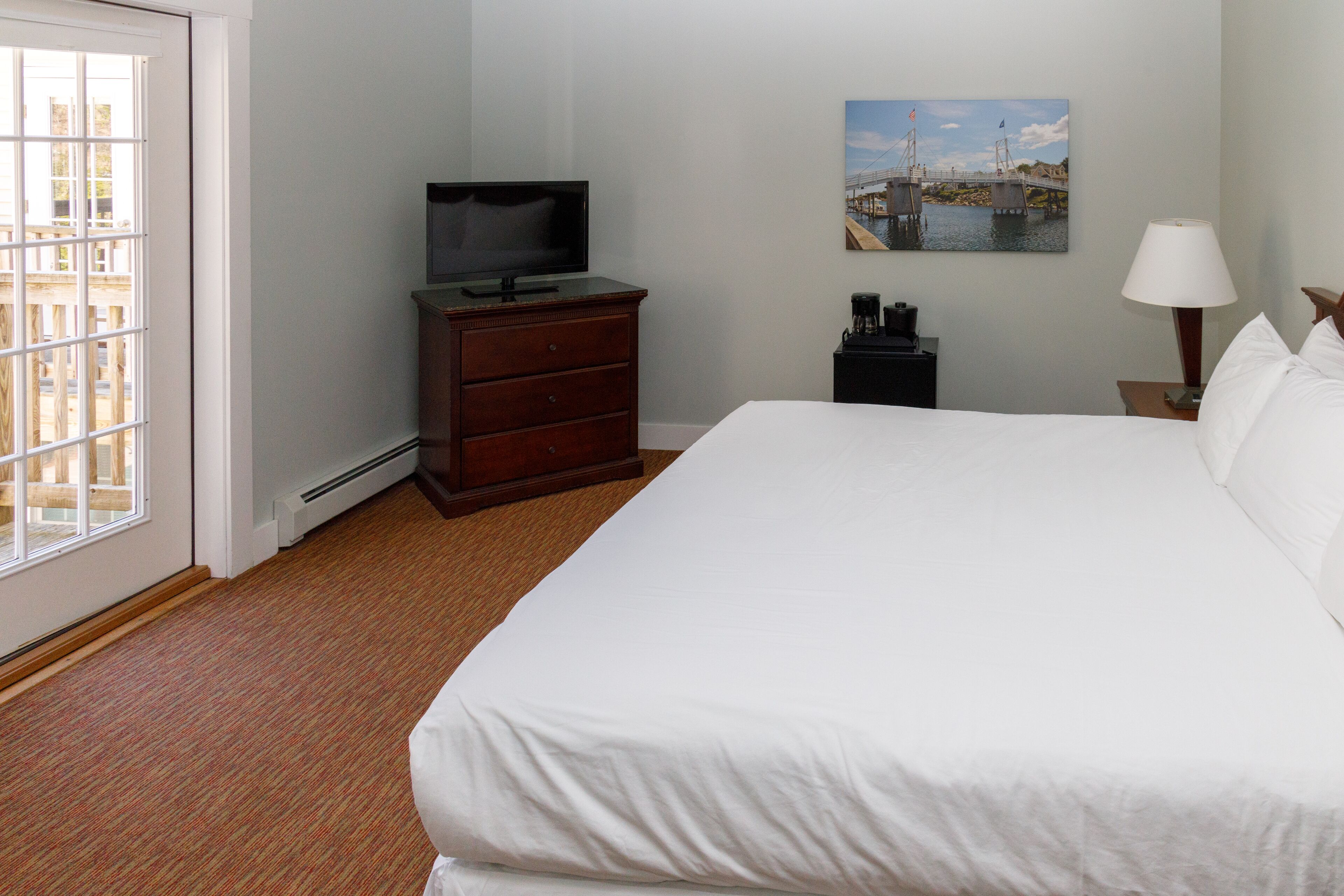 A hotel room with a large bed, a television on a dresser, a painting on the wall, and a window with a view of buildings.