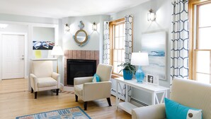 A living room with two armchairs, a coffee table, a fireplace, and a large window with patterned curtains. - The Admiral's Inn Resort (Ogunquit)