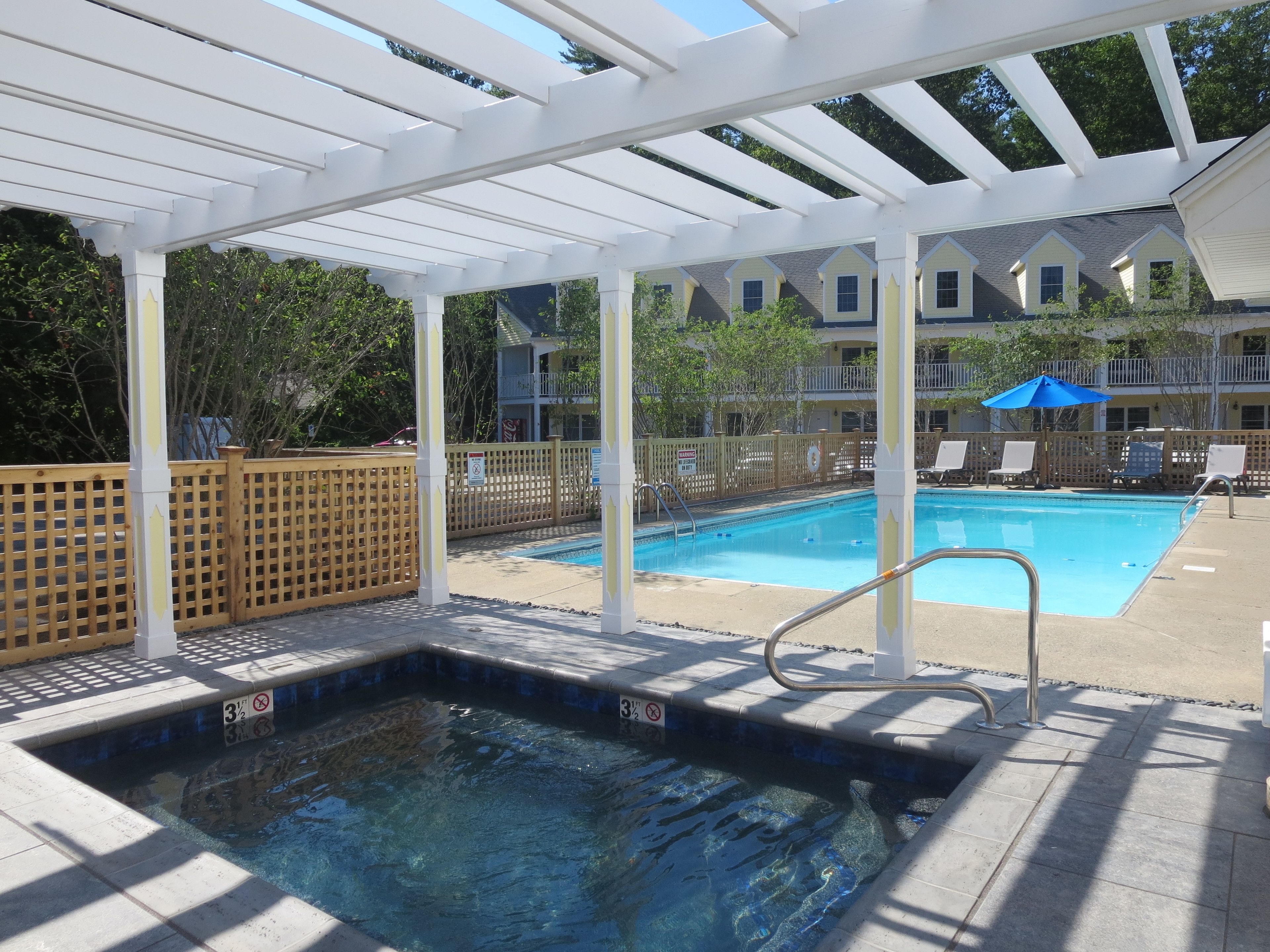 A pool area with a hot tub, lounge chairs, and a covered patio.