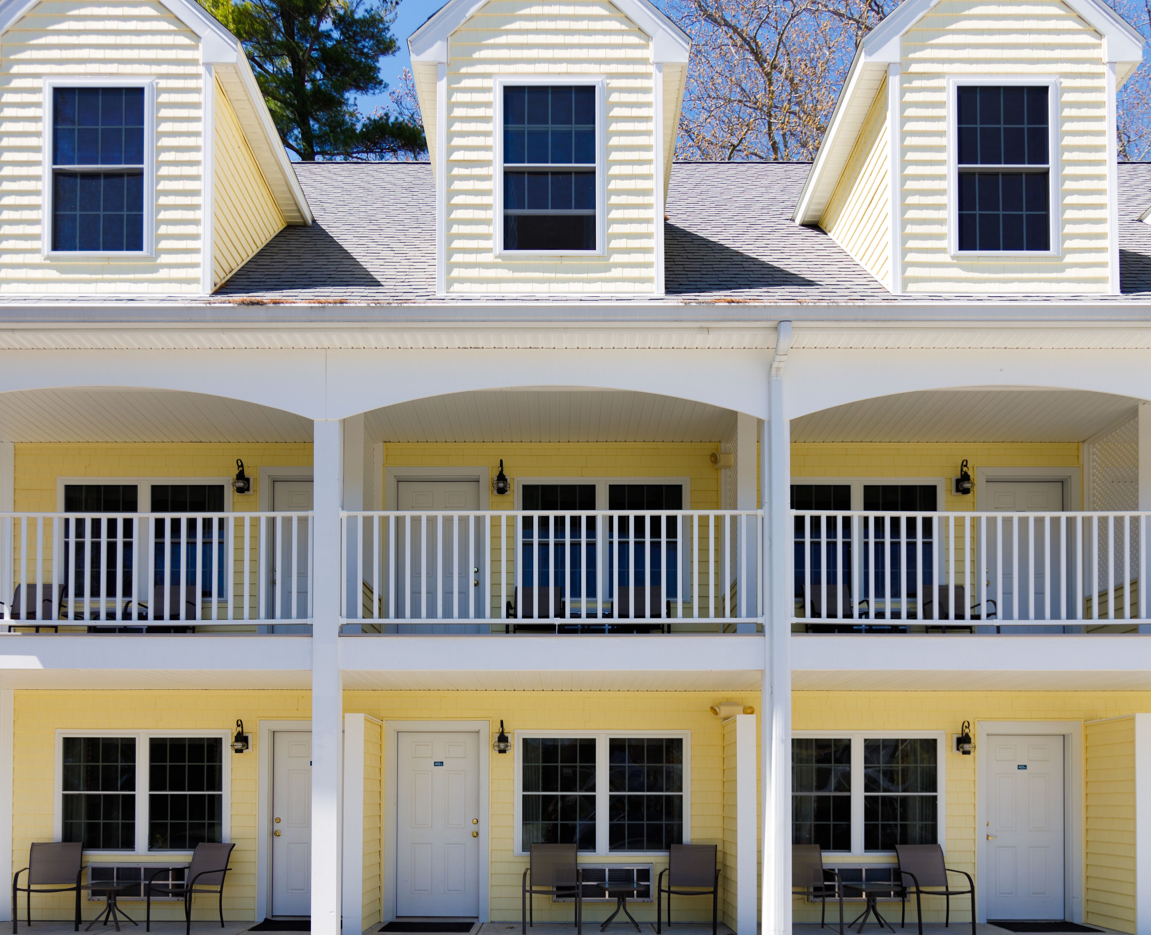 A three-story building with a yellow exterior, white trim, and a balcony on each floor.