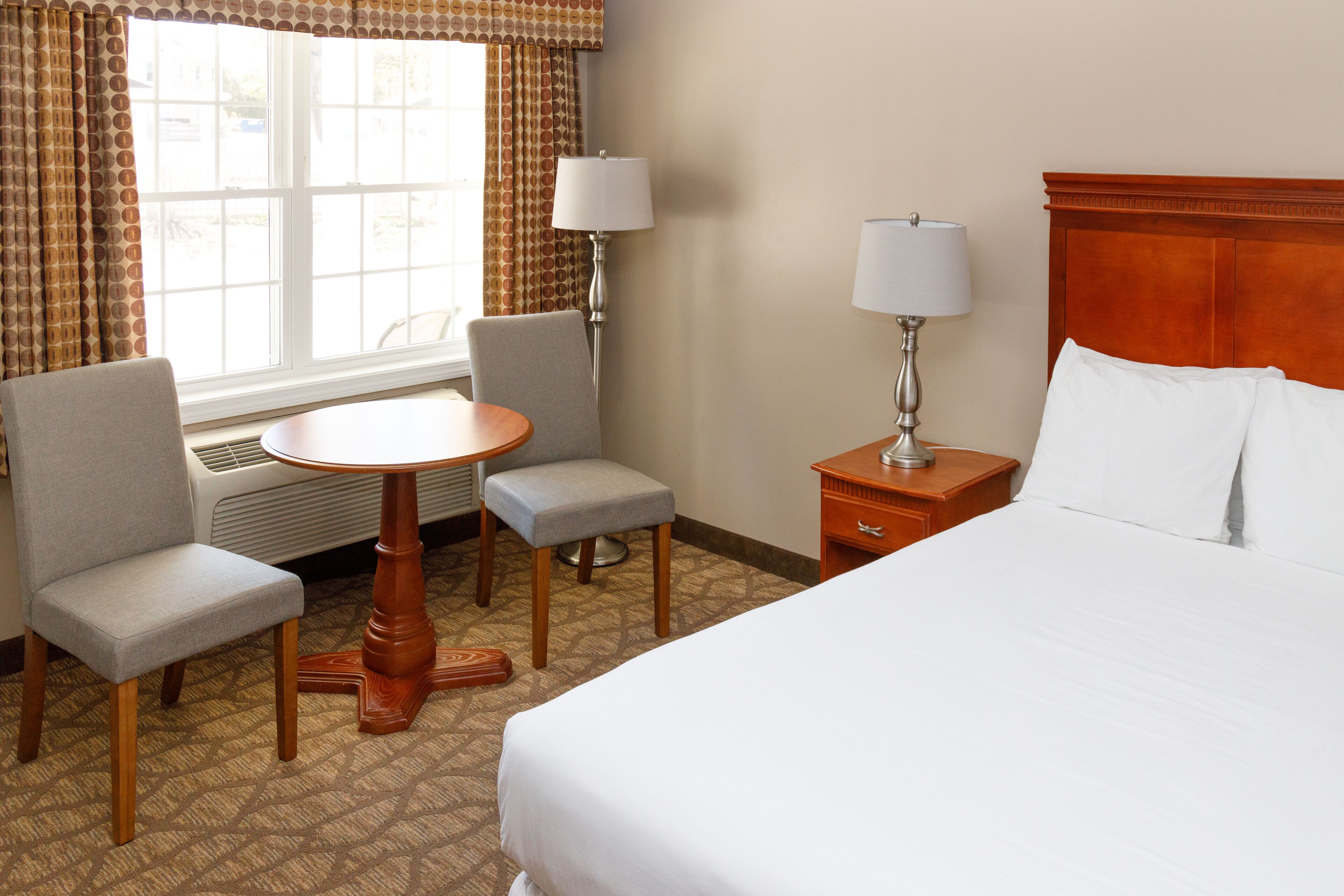 Una habitación de hotel con cama, escritorio, dos sillas, mesa y lámpara.