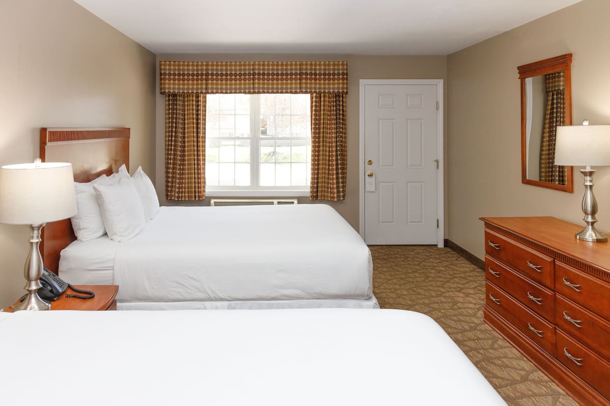 A hotel room with a large bed, a dresser, a bedside table with a lamp, a telephone, and a window with curtains.