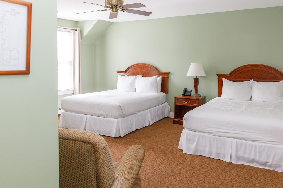 A hotel room with two beds, a ceiling fan, a nightstand with a lamp, and a framed picture on the wall.