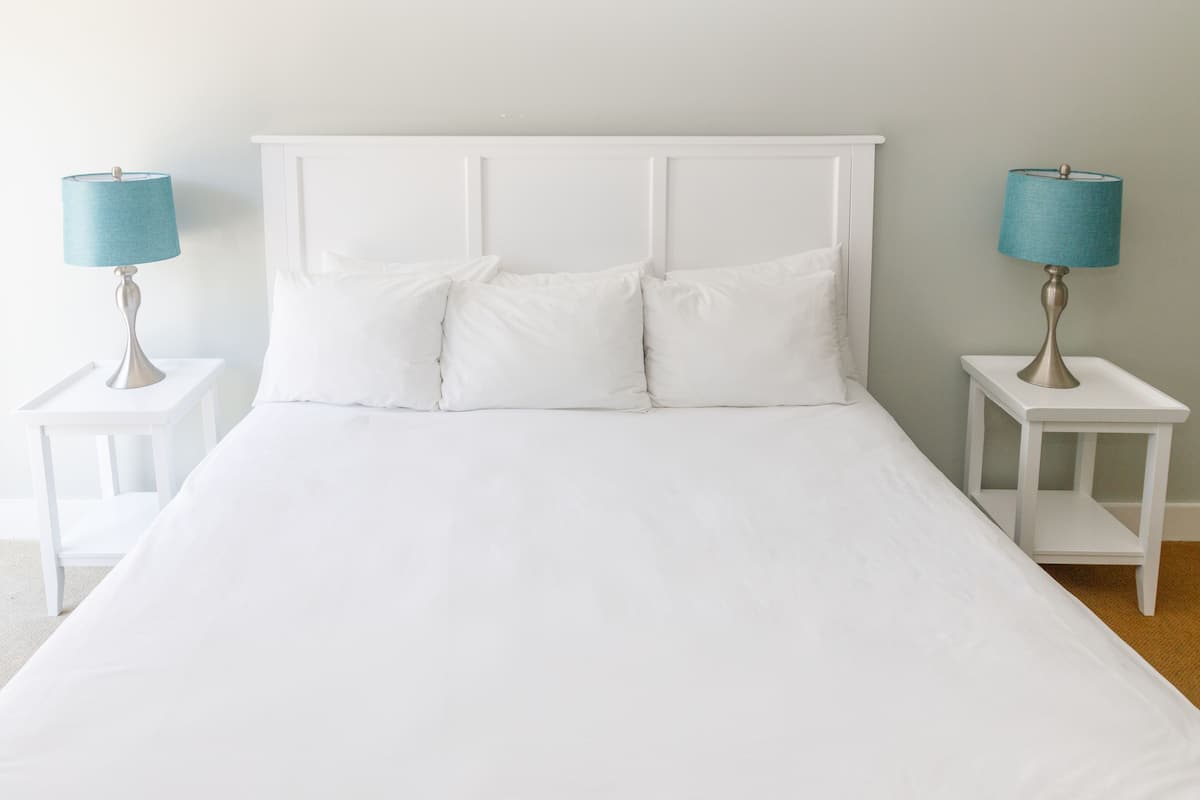 A neatly made bed with white bedding and two matching nightstands, each with a lamp.