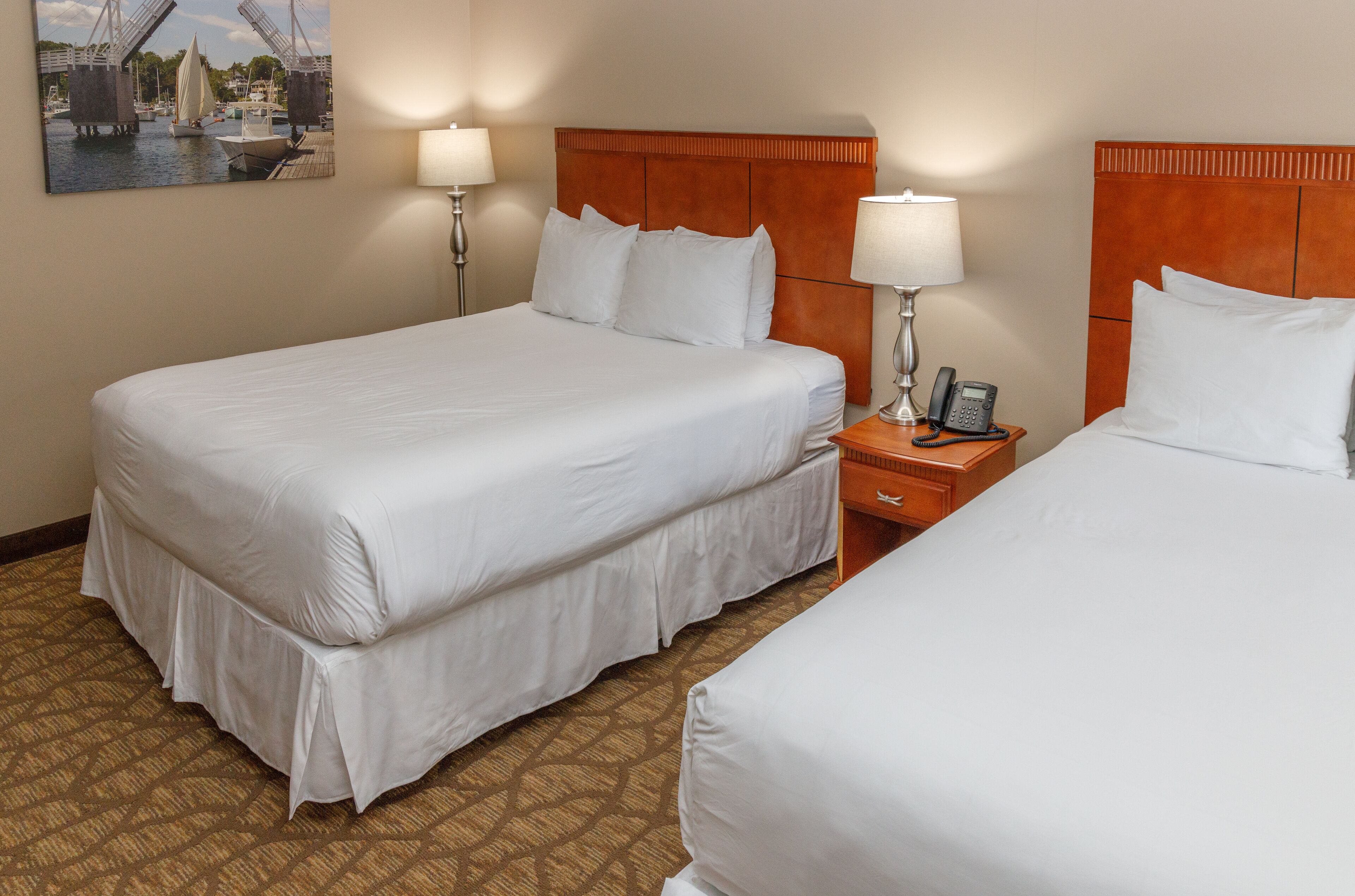A hotel room with two beds, a wooden headboard, bedside lamps, and a telephone on a nightstand.