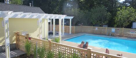 A backyard with a swimming pool, a covered patio, and a wooden fence.