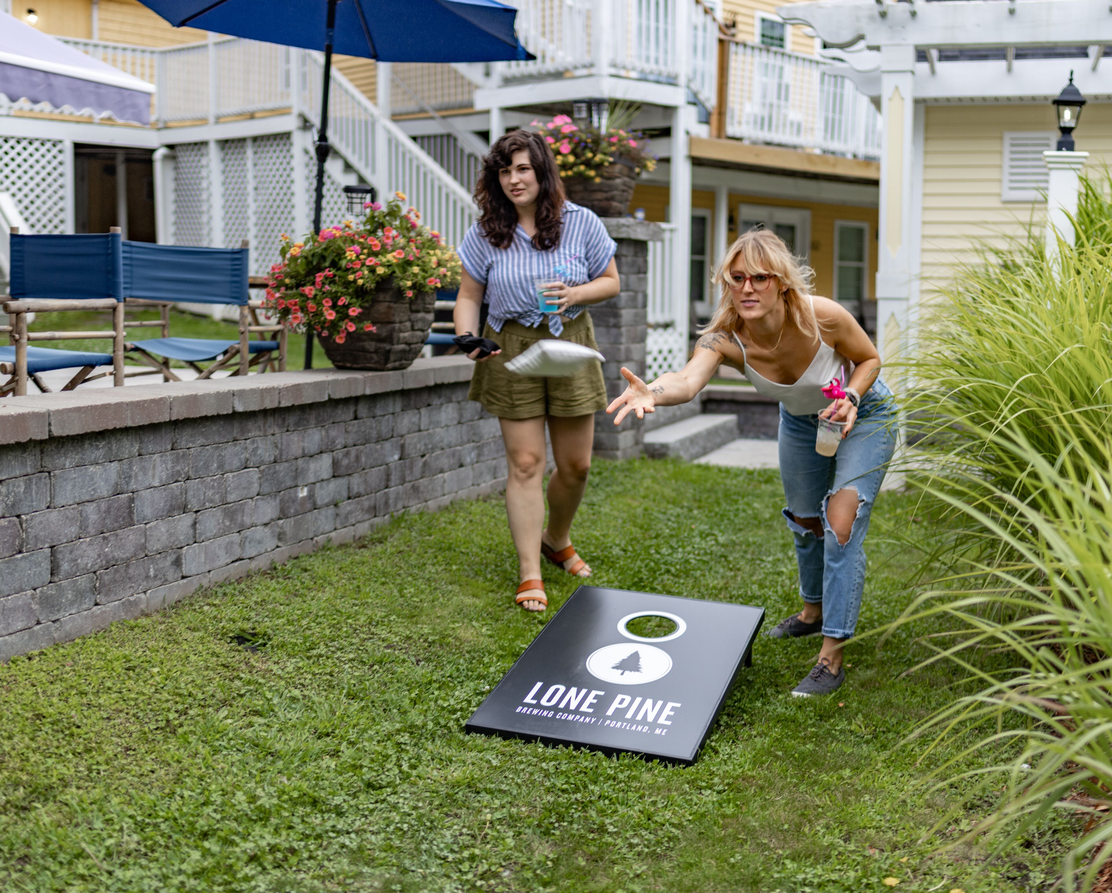 A woman playing a game on a lawn with a board labeled "Lone Pine Brewing Company Portland, ME."