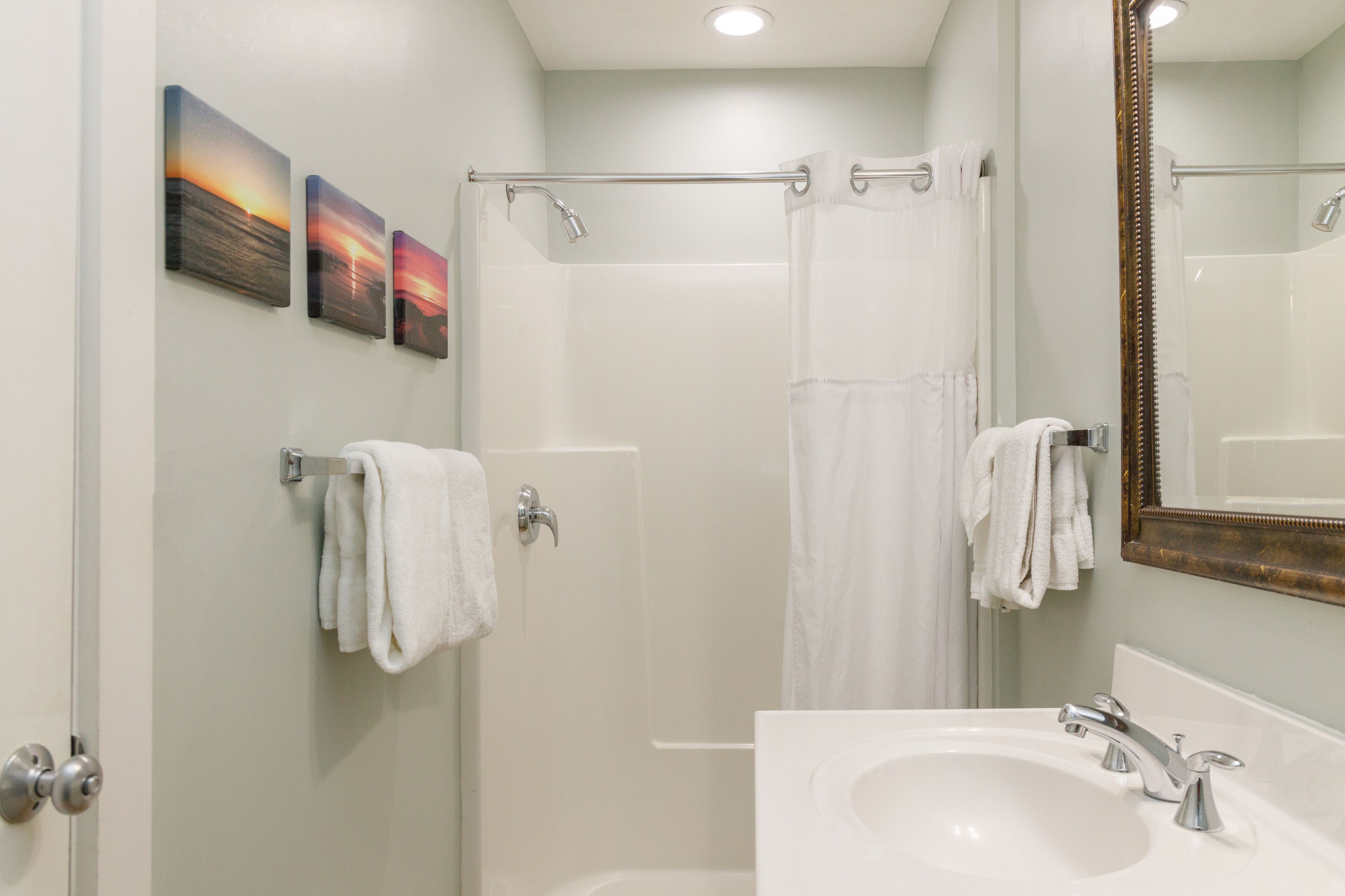 Un baño con un lavabo blanco, una ducha con puerta de cristal y tres cuadros colgados en la pared.