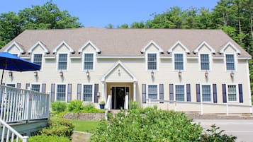 A two-story building with a symmetrical facade, a front porch with a white railing, and a blue umbrella.