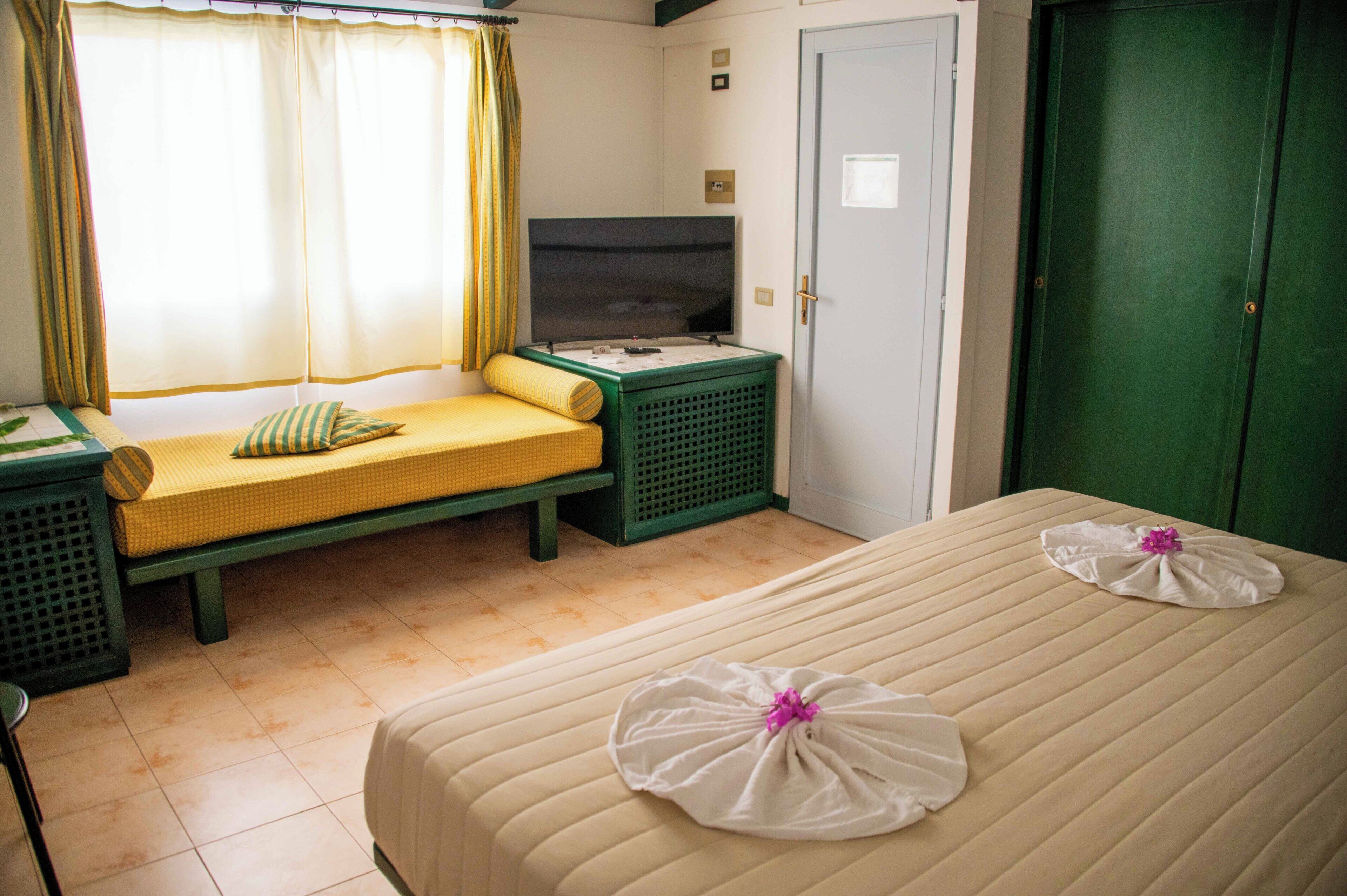 Habitación de hotel con dos camas, un banco, un televisor y un armario verde.