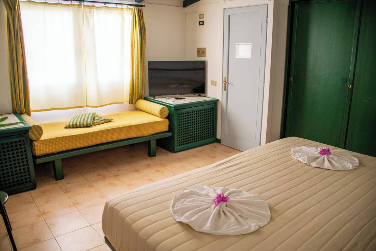 Een hotelkamer met een bed, een bankje, een televisie en een groene garderobe.