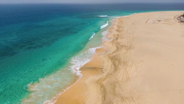 Vista aérea de una playa con aguas turquesas cristalinas y una orilla arenosa.