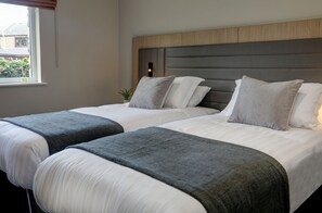 A hotel room with two beds, each with white linens and grey throw blankets.