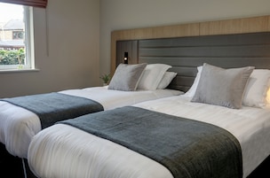 Habitación de hotel con dos camas, cada una con ropa de cama blanca y mantas grises.