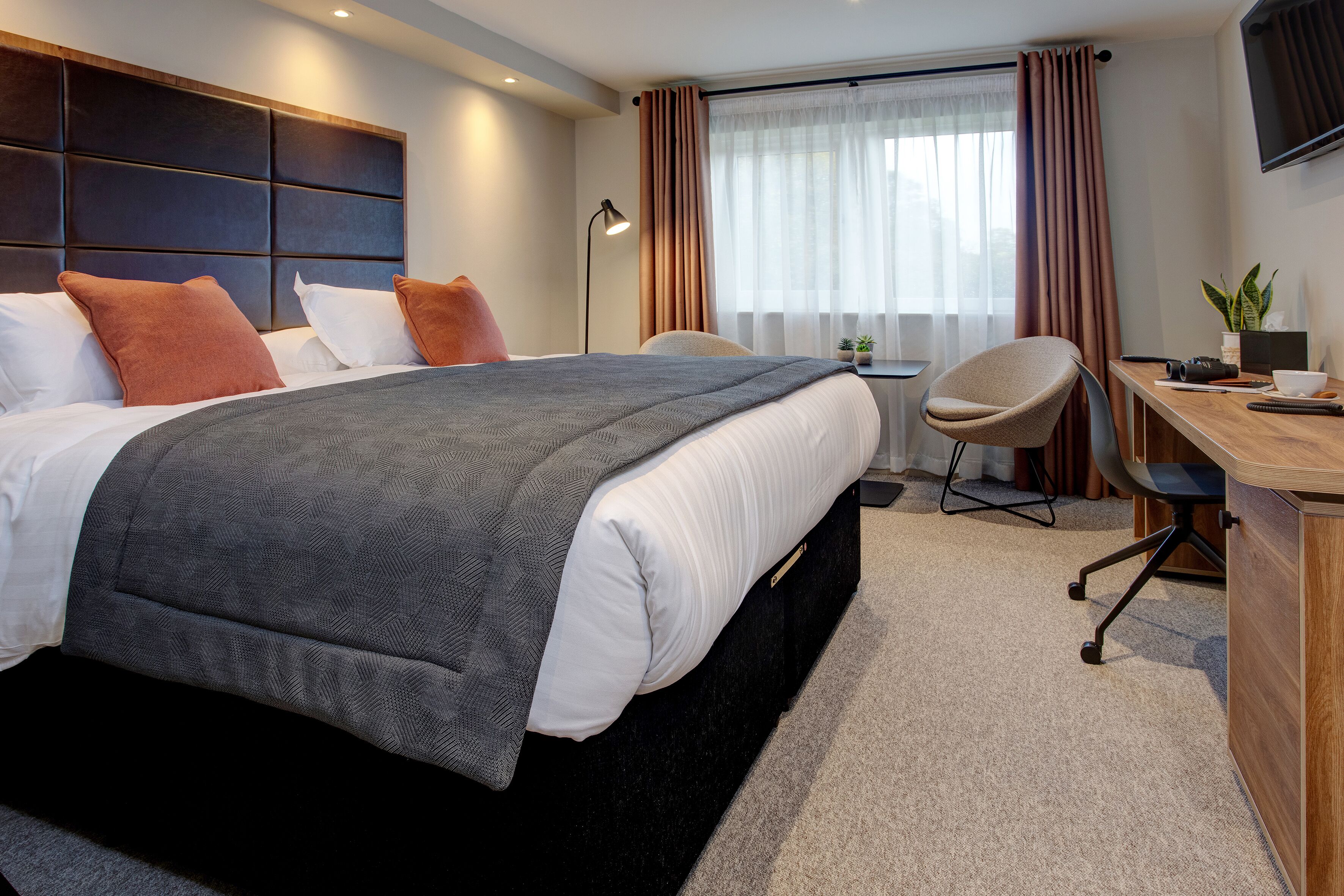 A modern hotel room with a large bed, a desk, and a chair.