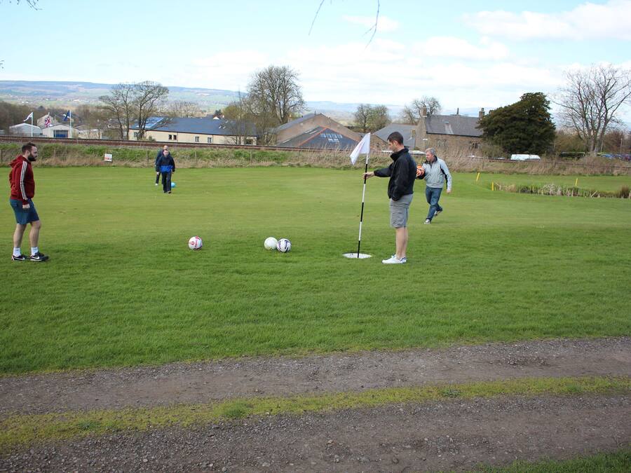 A grassy field with a flagstick, a golf ball, and a person in a blue jacket.