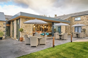 A modern outdoor patio area with stone walls, wicker furniture, and umbrellas providing shade. - Mytton Fold Hotel (Blackburn)
