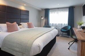 A hotel room with a large bed, a desk, a chair, and a TV.