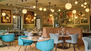 Ein Restaurant mit blaugrünen Stühlen und Tischen, Holzboden im Fischgrätmuster und verschiedenen gerahmten Kunstwerken an den Wänden.