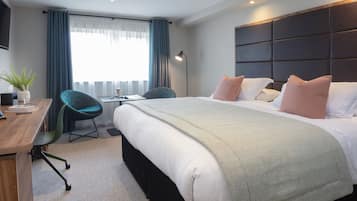 Quarto de hotel com uma cama grande, uma mesa, uma cadeira e uma janela com cortinas.