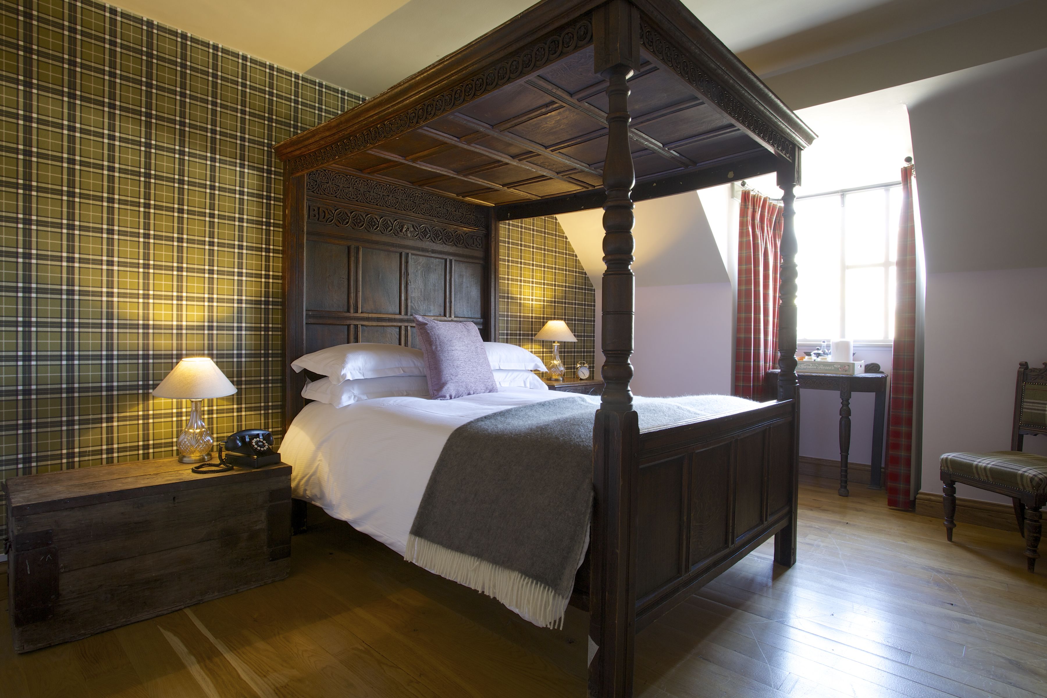Un lit à baldaquin avec une tête de lit en bois, une table de chevet avec une lampe et un mur orné d’un motif à carreaux.