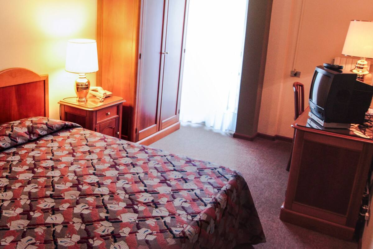 Une chambre d’hôtel comprenant un lit, une table de chevet avec une lampe, un téléviseur et une armoire.