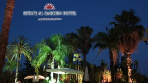 A nighttime view of the ESTATE AL GARDEN HOTEL's outdoor area with palm trees, lounge chairs, and a pool area. - Garden Hotel (San Giovanni la Punta)