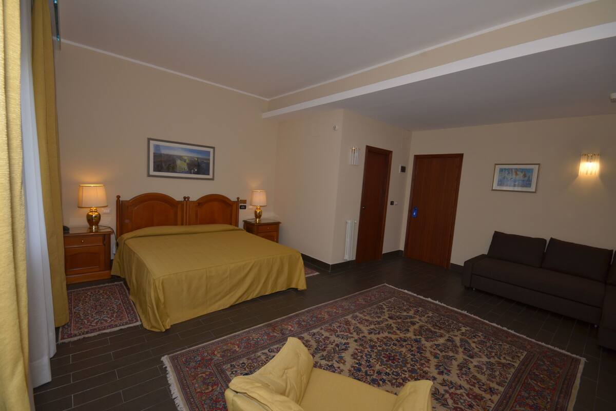 Une chambre d’hôtel avec un grand lit, un canapé, deux tables de chevet avec des lampes, une moquette et deux portes.