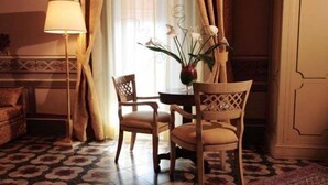 A room with a patterned floor, a wooden table with chairs, a vase with flowers, a lamp, and curtains. - Hotel Manganelli Palace (Catania)