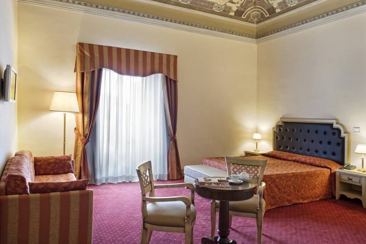 Una habitación de hotel con cama, escritorio, silla, sofá y mesita de noche.