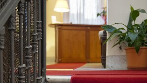 A hotel entrance with a red carpet leading to a wooden counter and a potted plant. - Hotel Manganelli Palace (Catania)