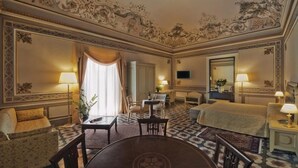 A hotel room with a large bed, a dining table, two chairs, a sofa, a TV, and a decorative ceiling. - Hotel Manganelli Palace (Catania)