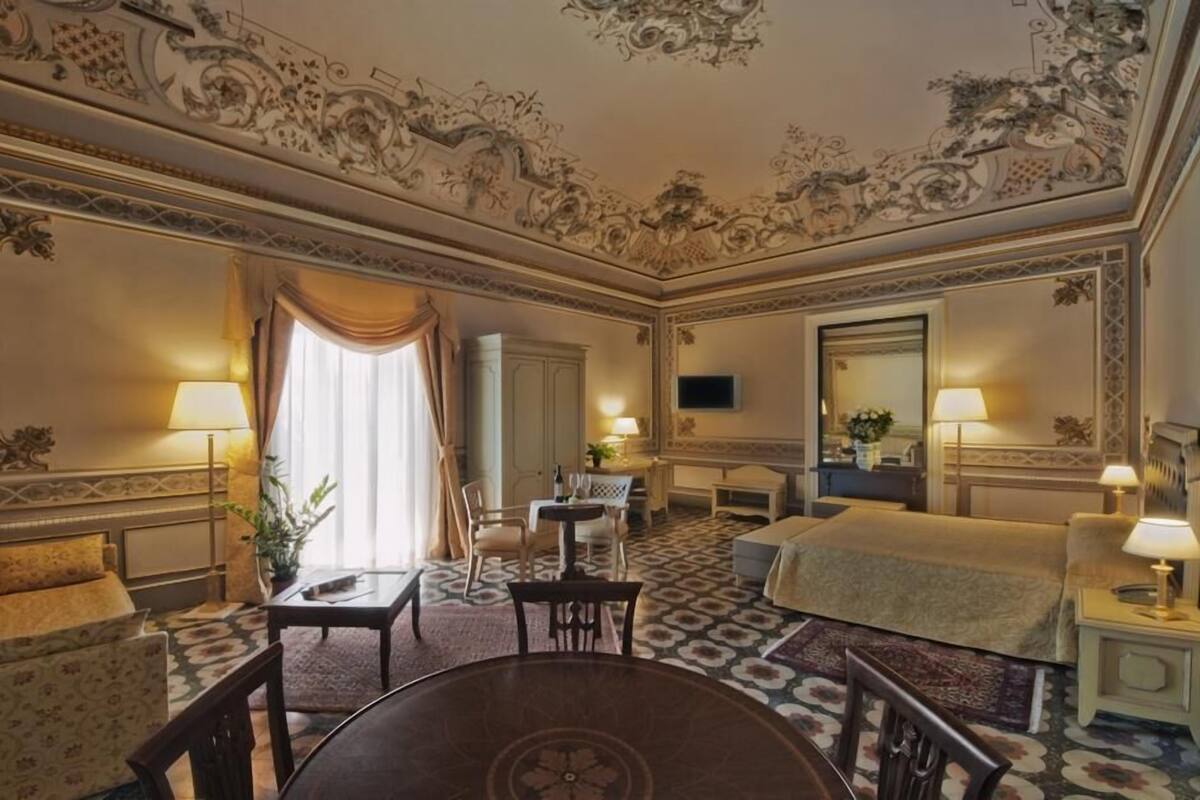 Habitación de hotel con una cama grande, una mesa de comedor, dos sillas, un sofá, un televisor y un techo decorativo.