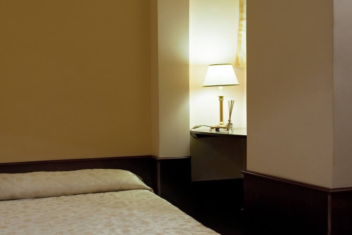 Una habitación de hotel con cama, mesita de noche y lámpara.