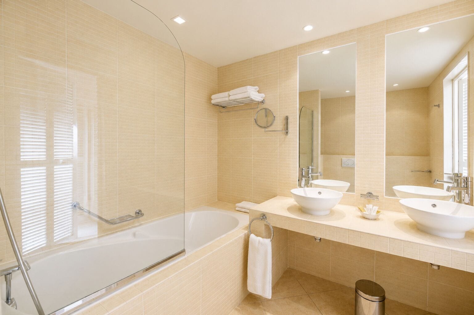 A modern bathroom with a bathtub, two sinks, a large mirror, and a towel rack.