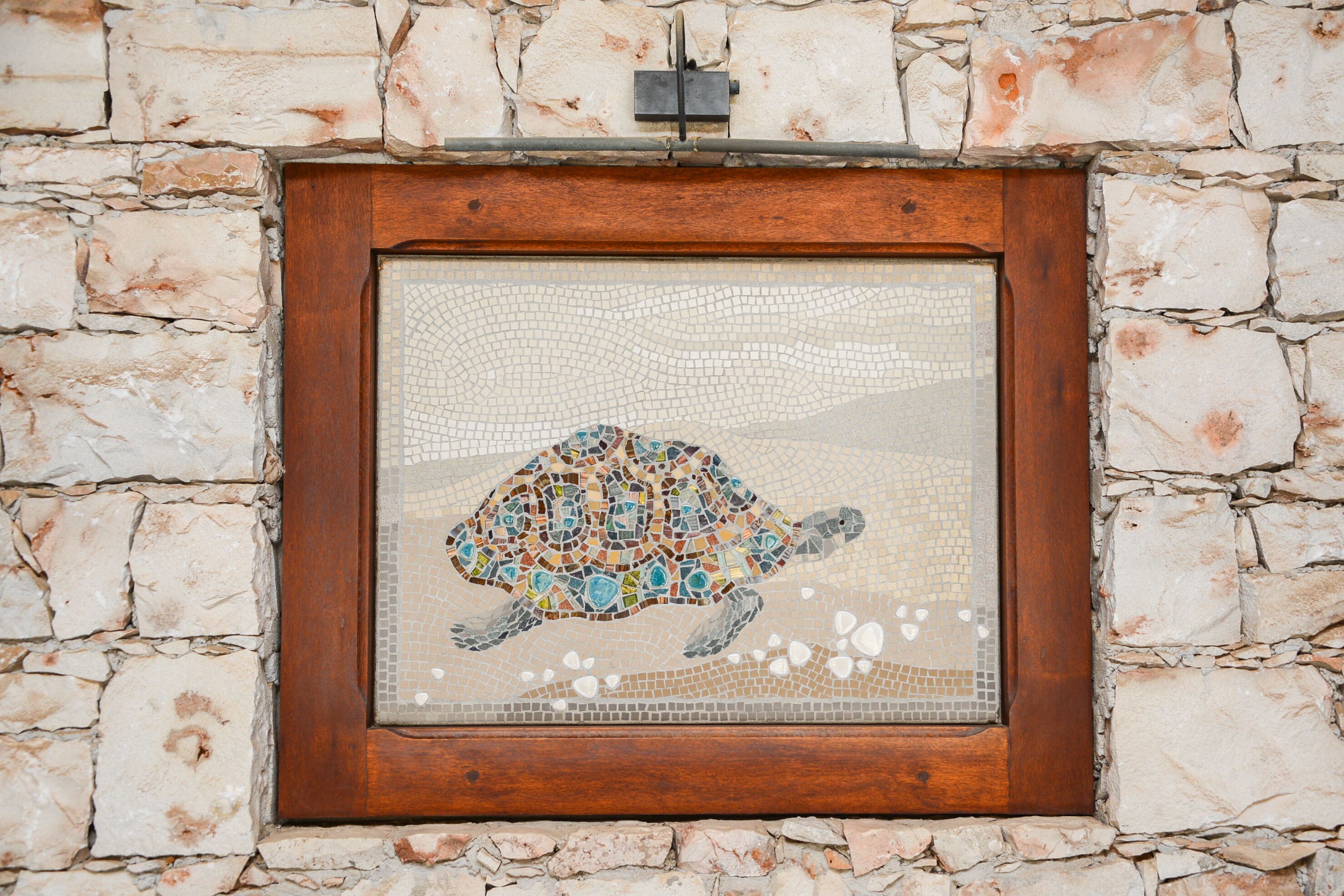 A framed mosaic of a turtle on a stone wall.