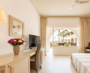 A hotel room with a desk, television, and a view of the outdoor seating area. - Morabeza Hotel (Sal)