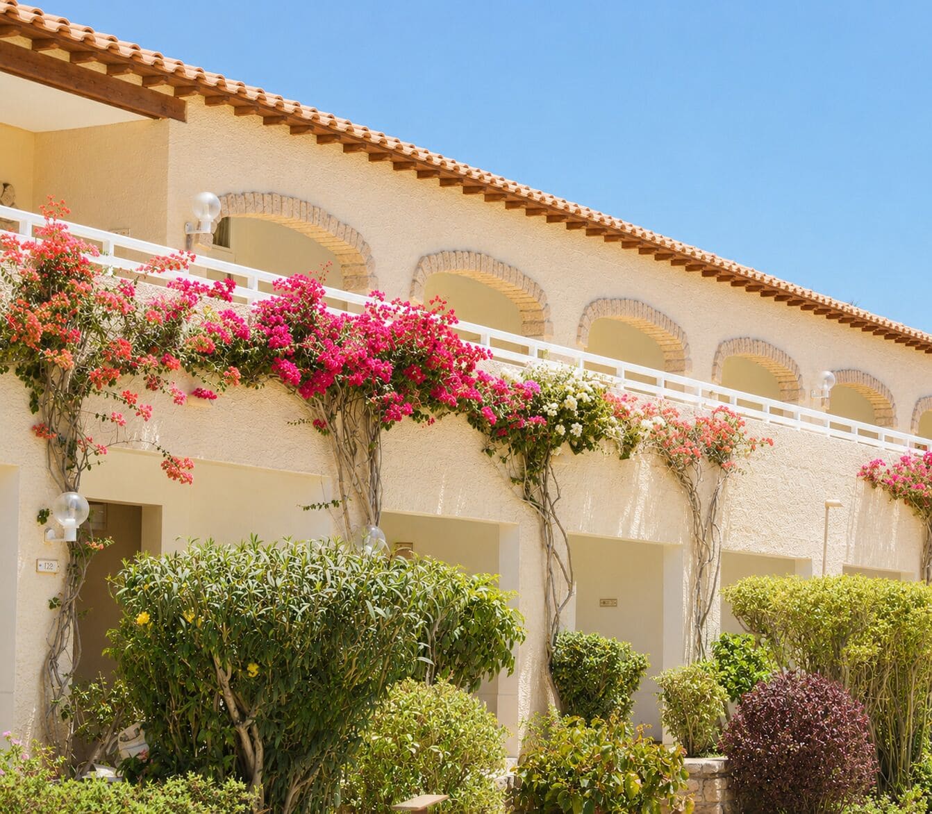 A building with a terracotta roof, arched windows, and a balcony with pink bougainvillea.