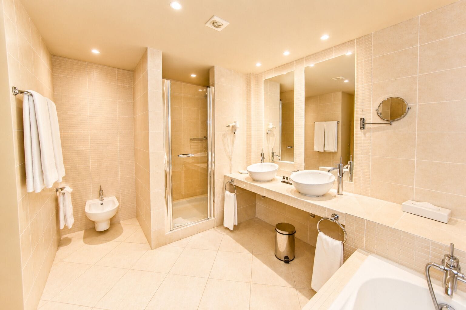 Un baño moderno con ducha a ras de suelo, dos lavamanos, un bidé y un espejo grande.